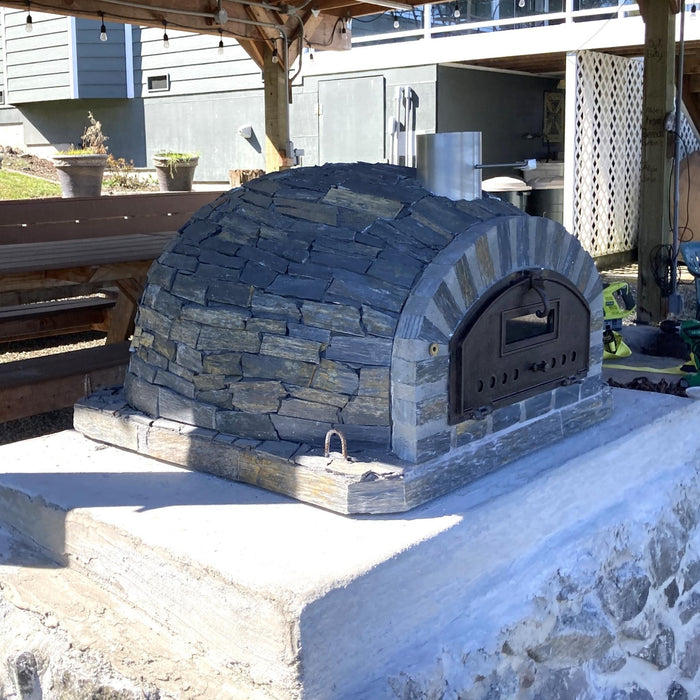 Rustic Pizzaioli Premium Pizza Oven by Authentic Pizza Ovens in stacked stone finish, shown from side angle on outdoor countertop