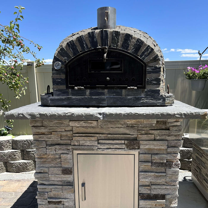 Rustic Pizzaioli Premium Pizza Oven by Authentic Pizza Ovens front view installed on stacked stone base outdoors.