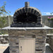 Rustic Pizzaioli Premium Pizza Oven by Authentic Pizza Ovens front view installed on stacked stone base outdoors.